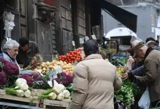 man in brown coat standing in front of fruit stand