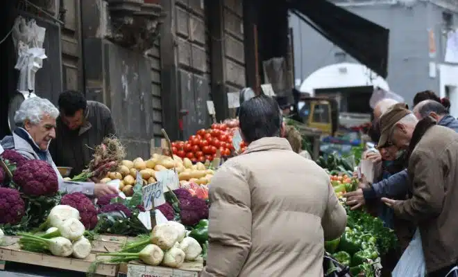 man in brown coat standing in front of fruit stand